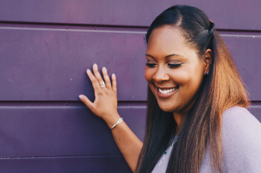 Woman with Invisalign smiling against a wall